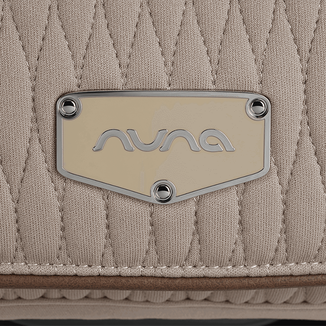 Beige quilted nuna brand patch with silver logo and rivets on nuna arra flex car seat cosmopolitan i size baby seat