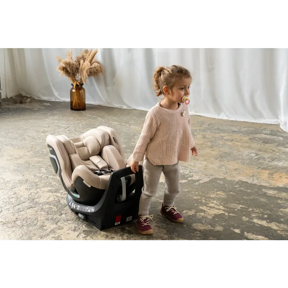 Child with a dummy standing beside an Elegant Beige Recaro XENON 1 on a concrete floor.