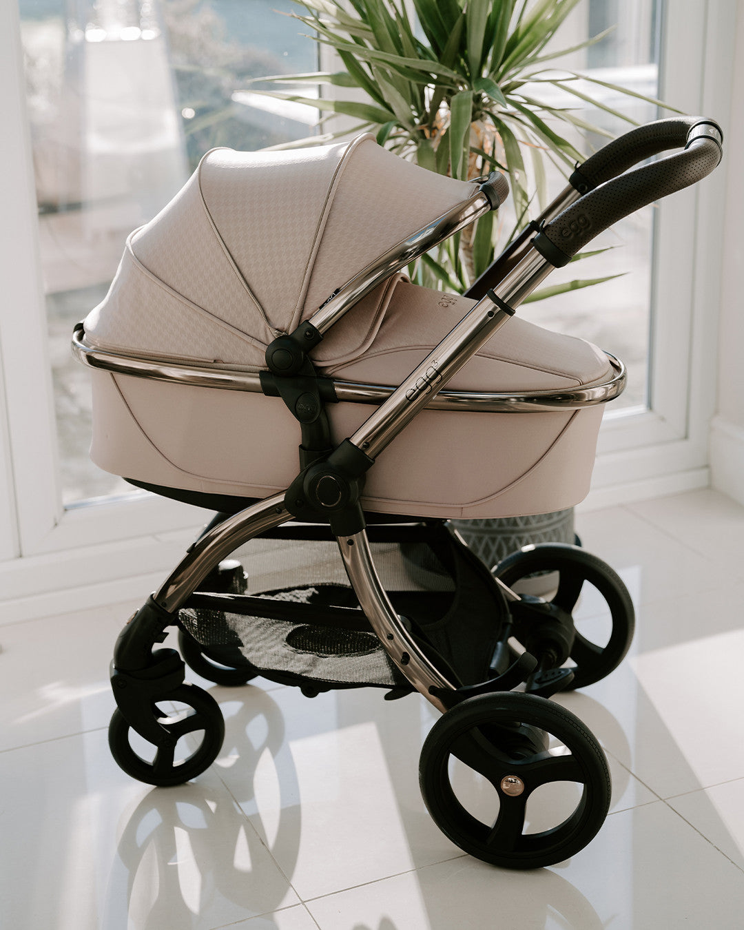 A sleek, blush-colored pram with a metallic frame and black wheels.