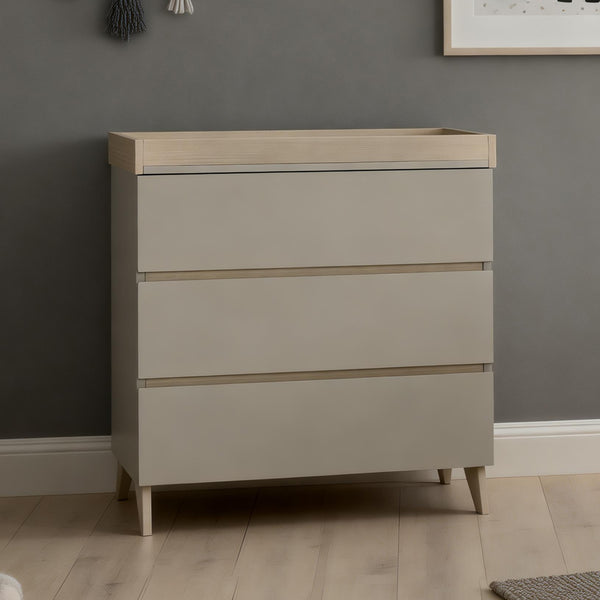 Beige three-drawer changing table with light wood accents and tapered legs from babymore dante nursery set