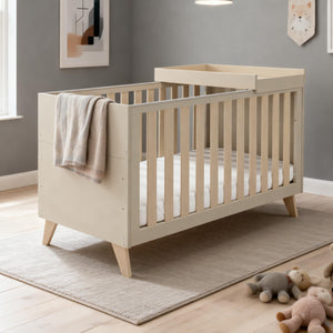 Beige wooden Babymore Dante cot bed with cot top changer featuring slatted sides and angled legs in cashmere finish