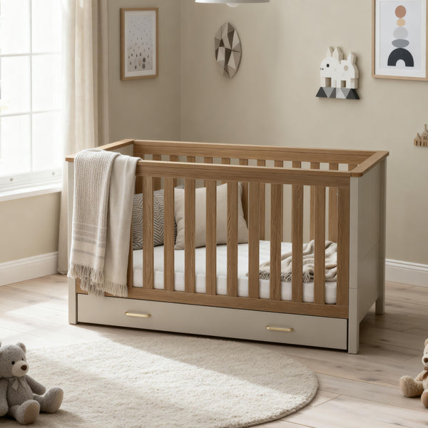 Babymore Mira cot bed in cashmere warm oak with light wood finish, vertical slats, and matching drawer base
