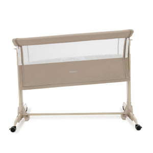 Beige babymore neera bedside crib with mesh sides and caster wheels for safe and portable infant sleep