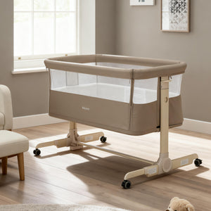 Beige fabric babymore neera bedside crib with mesh sides and wheeled base for easy mobility