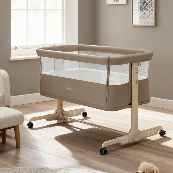 Beige fabric babymore neera bedside crib with mesh sides and wheeled base for easy mobility