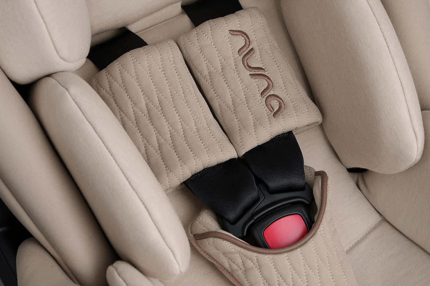 Beige quilted fabric seat belt cover with embroidered ’nuu’ logo.
