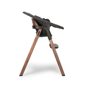 Nuna BRYN highchair with sleek black frame wooden legs warm brown finish and textured gray fabric seat in sanderson color