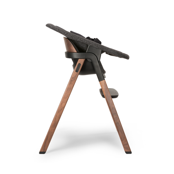 Nuna BRYN highchair with sleek black frame wooden legs warm brown finish and textured gray fabric seat in sanderson color
