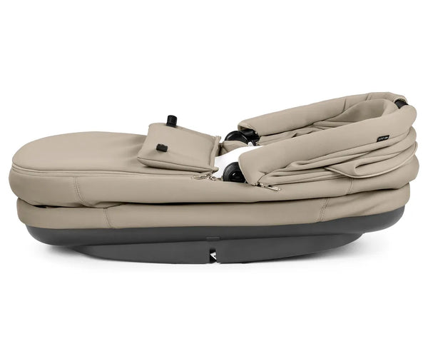Beige fabric-lined peg perego city loop pro baby bassinet with black plastic base and wheels in vanilla blend color