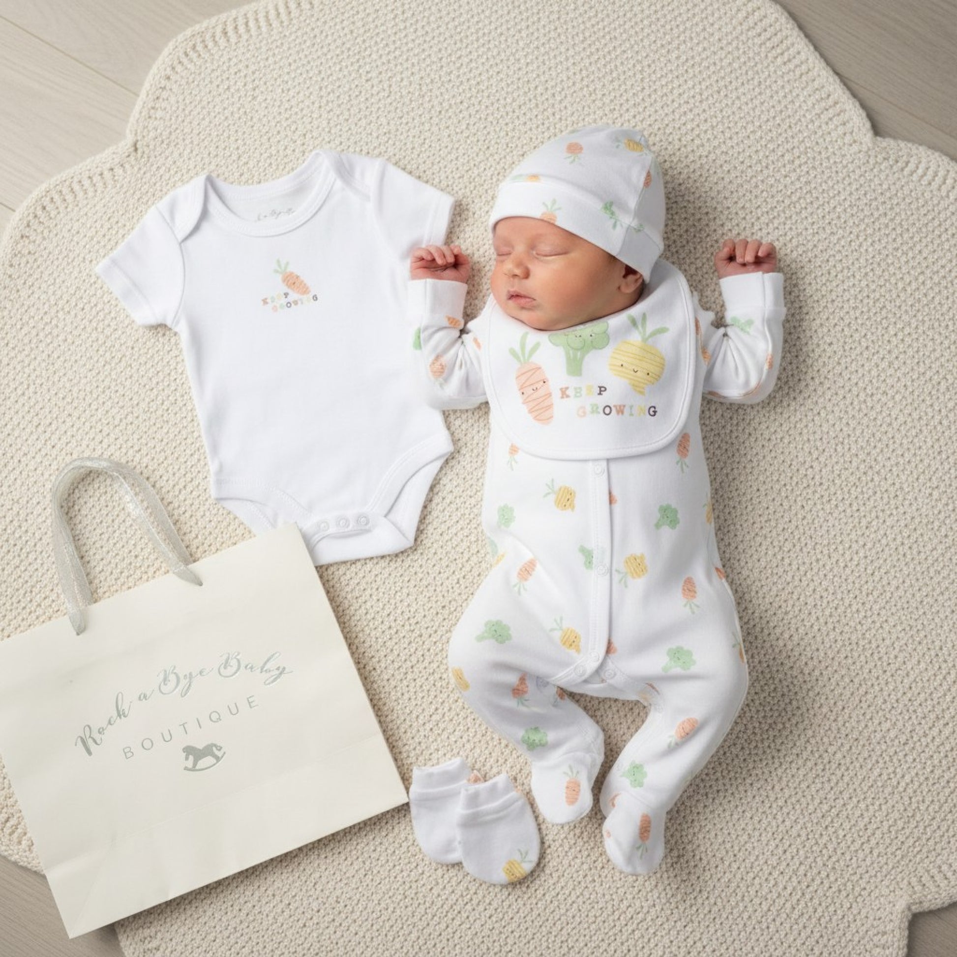 A baby wearing the unisex baby keep growing 5 piece layette set in white with colorful carrot and pineapple prints