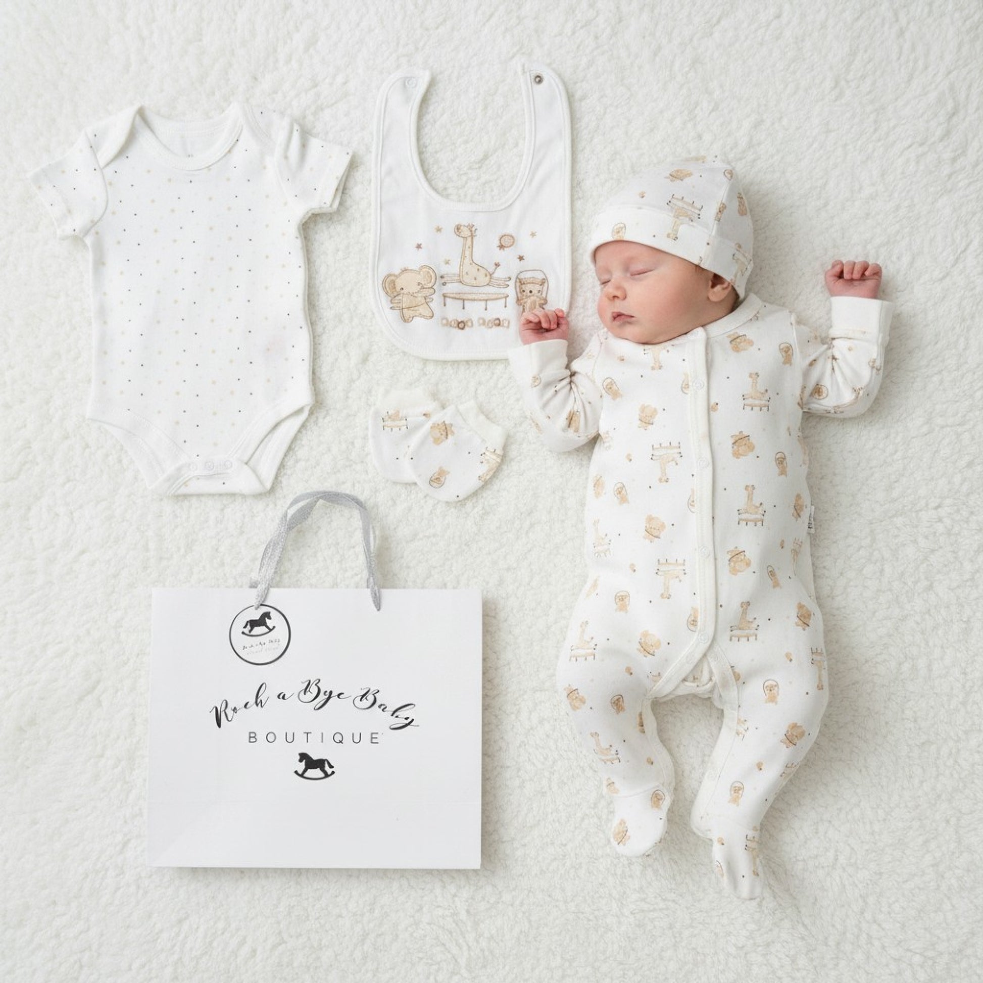 A sleeping baby wearing a white cotton unisex play time 5 piece layette set with beige animal prints and matching hat and bib