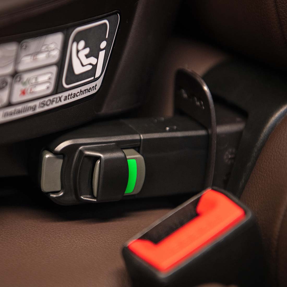 Black plastic car seat belt buckle with green indicator light and orange release button on nuna base curv isofix base