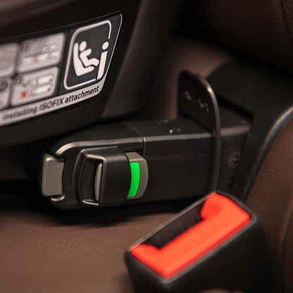Black plastic car seat belt buckle with green indicator light and orange release button on nuna base curv isofix base