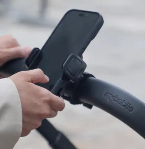Black smartphone mounted in a sleek, adjustable clamp on the handlebar of a mybablie stroller.