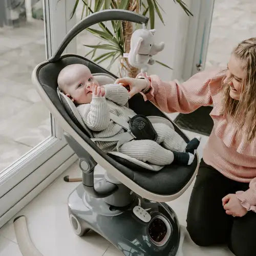 Gray and white baby swing with a plush elephant toy hanging above