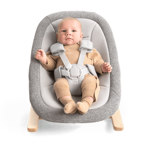 Gray textured fabric nuna bryn newborn rocker with light wood legs and adjustable safety straps for infants