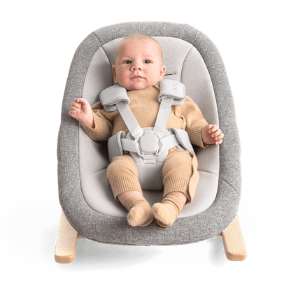 Gray textured fabric nuna bryn newborn rocker with light wood legs and adjustable safety straps for infants