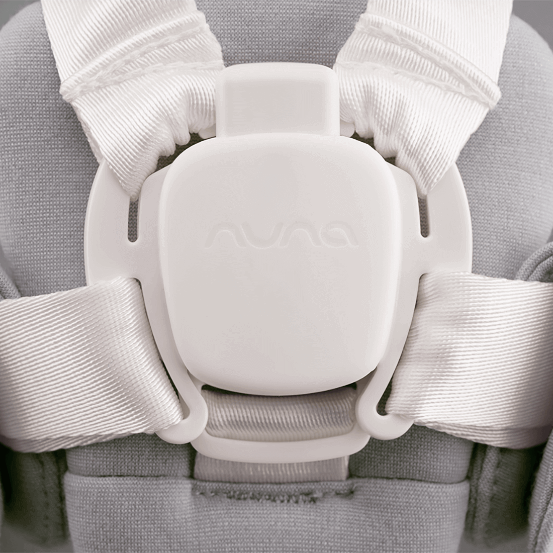 White plastic buckle with embossed logo securing white ribbed fabric straps on nuna bryn newborn rocker heritage