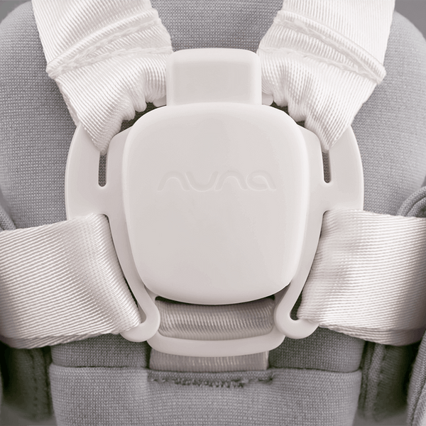 White plastic buckle with embossed logo securing white ribbed fabric straps on nuna bryn newborn rocker heritage