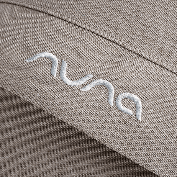 Beige textured fabric with white embroidered nuna logo on nuna mixx next stroller chateau seat upholstery
