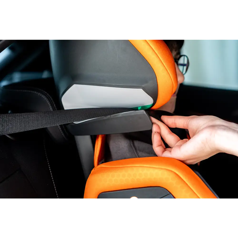 Close-up of a hand positioning the vehicle seat belt beneath the Vibrant Orange AXION 1 headrest.