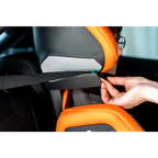 Close-up of a hand positioning the vehicle seat belt beneath the Vibrant Orange AXION 1 headrest.