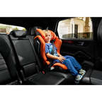Child seated in a Vibrant Orange AXION 1 in a vehicle, wearing a diagonal seat belt.