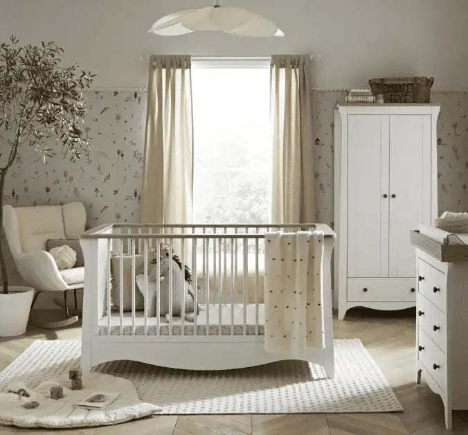  White wooden crib with curved sides and vertical slats, draped with a cream-colored blanket featuring subtle dark polka dots.